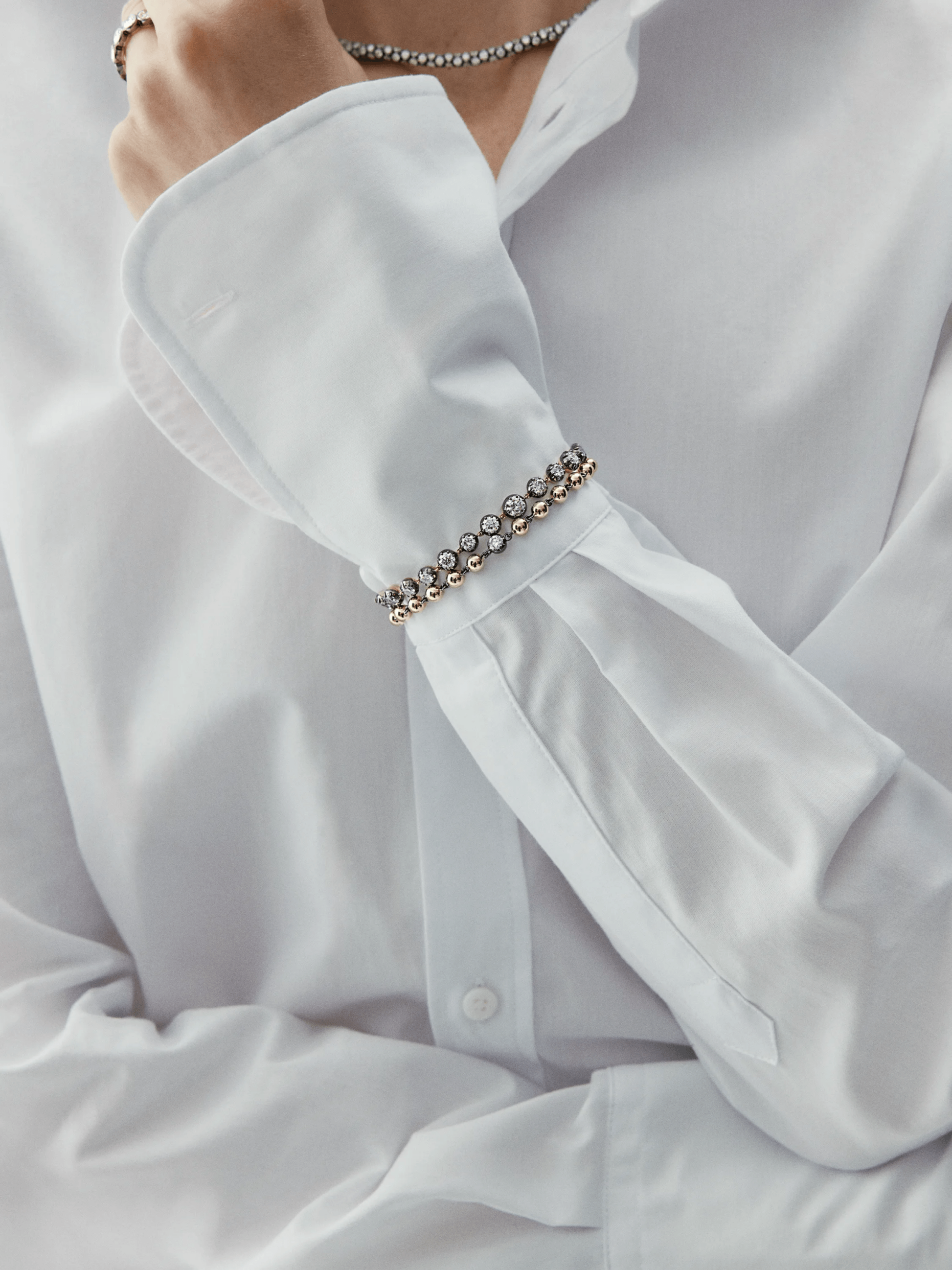 Close-up of a wrist adorned with a yellow gold diamond bracelet featuring round brilliant diamonds, styled with a crisp white shirt cuff. View 3