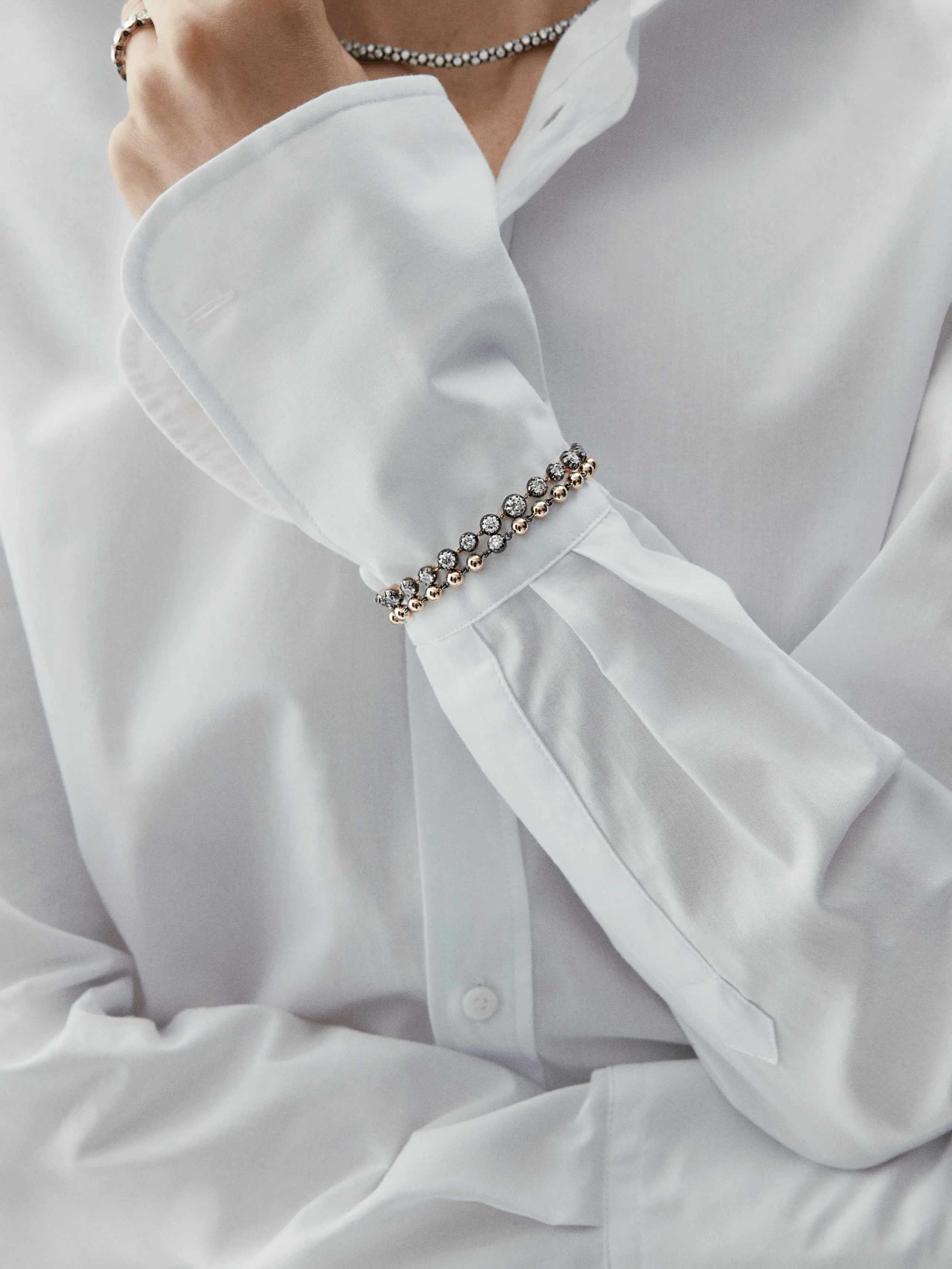 Close-up of a wrist adorned with a yellow gold diamond bracelet featuring round brilliant diamonds, styled with a crisp white shirt cuff. View 3