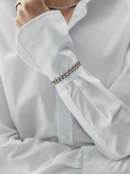 Close-up of a wrist adorned with a yellow gold diamond bracelet featuring round brilliant diamonds, styled with a crisp white shirt cuff. View 3