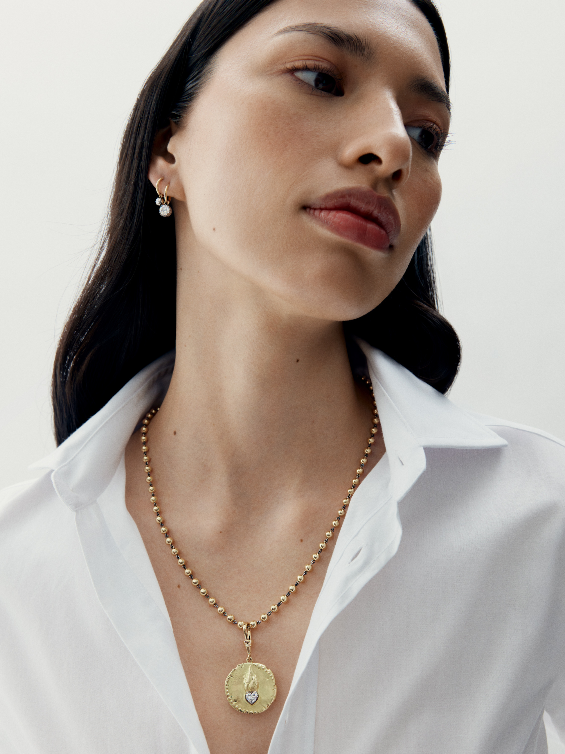 Woman wearing a gold necklace with a white shirt on a plain background View 3