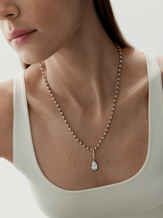Close-up of a woman wearing a delicate pear-shaped diamond pendant necklace with a ball chain in a contemporary, antique-inspired style. View 3