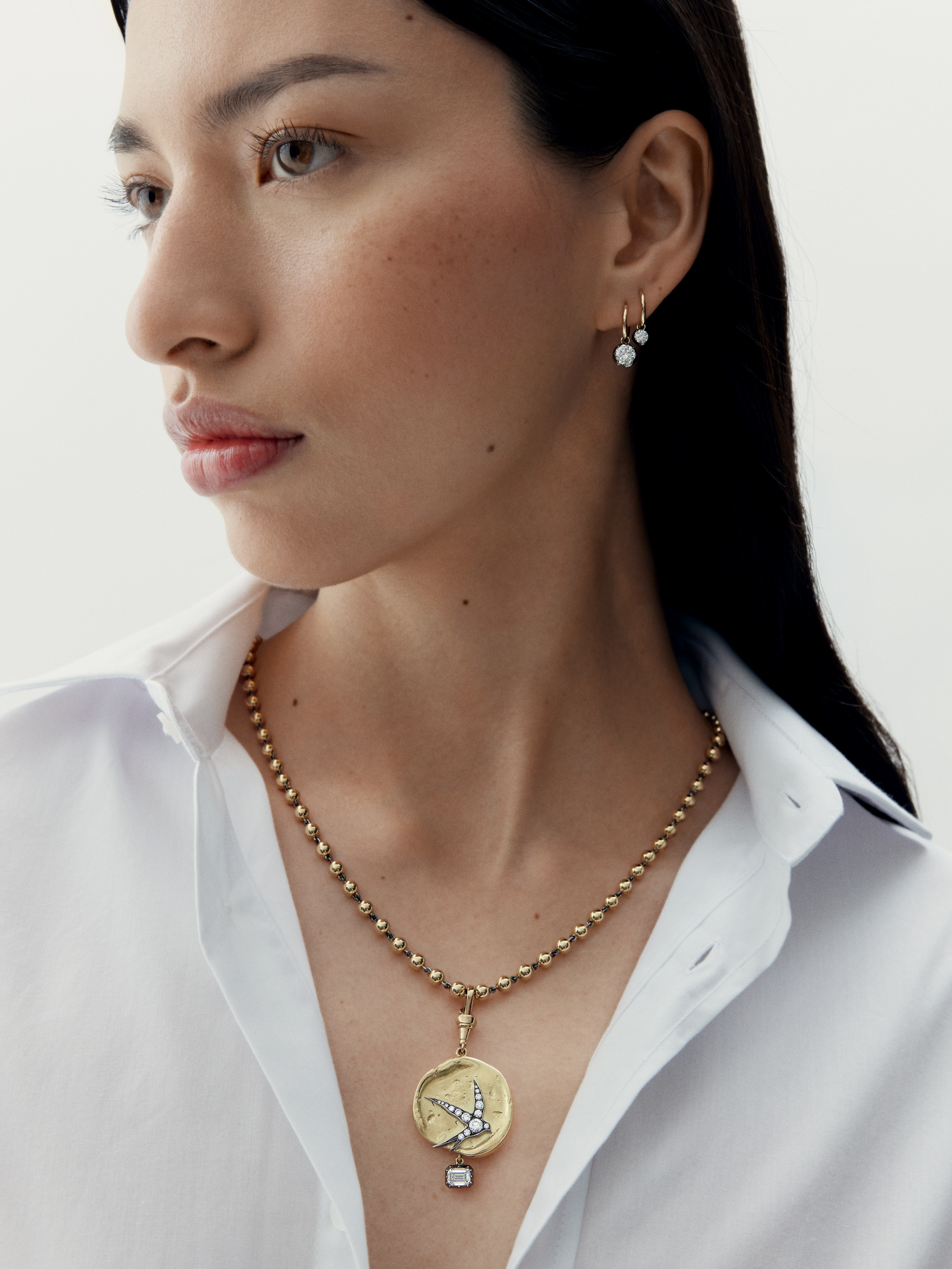 Woman wearing a gold necklace with a pendant on a plain background View 3