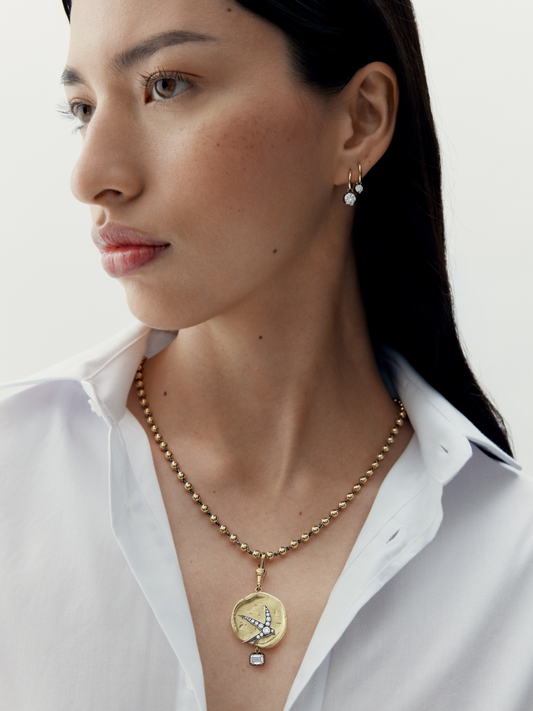 Woman wearing a gold necklace with a pendant on a plain background View 2