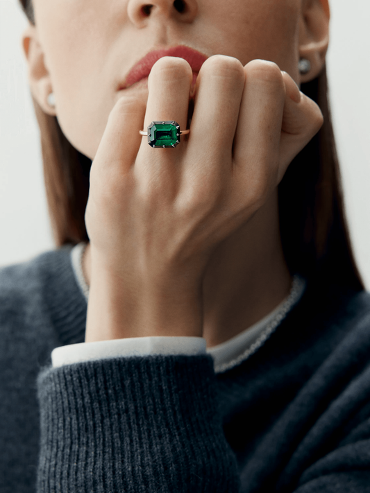 Close-up of a hand wearing an 18K white gold ring featuring a rectangular emerald cut green emerald, showcasing a blend of antique-inspired craftsmanship and contemporary design. View 3