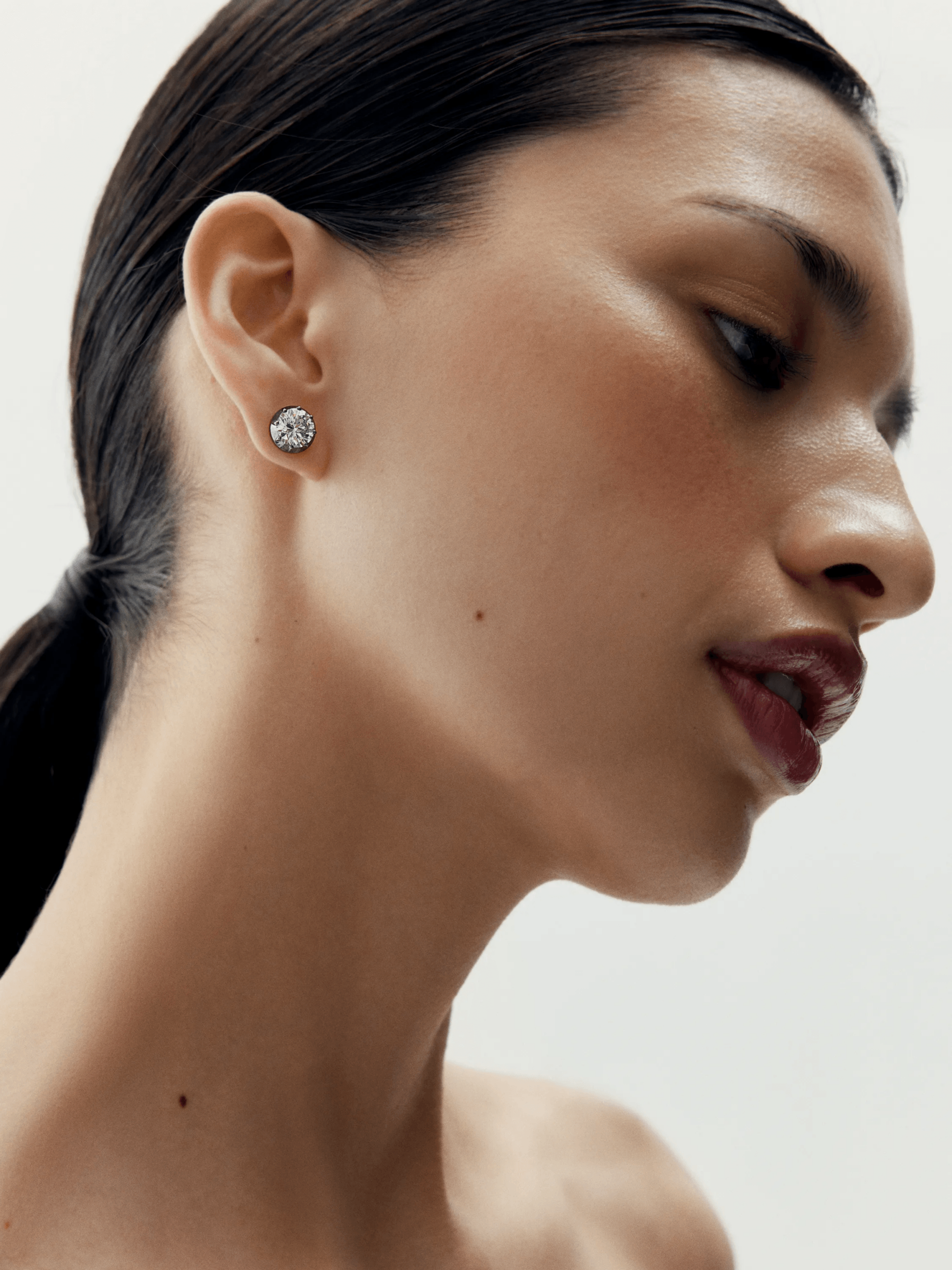Close-up view of a woman wearing understated diamond stud earrings set in blackened gold, showcasing a blend of antique-inspired craftsmanship and contemporary design. View 3