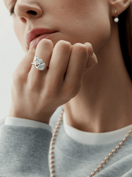 Close-up of a hand wearing a tilted pear-shaped diamond ring with a minimalist gold band, showcasing timeless craftsmanship and contemporary elegance.