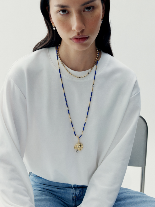 Woman wearing a long necklace with a white sweater and blue jeans on a light background View 2