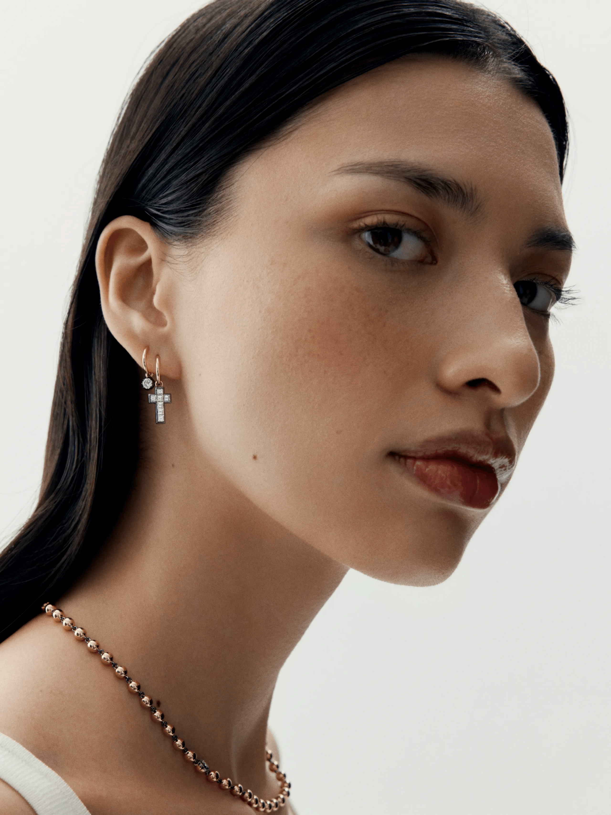 Close-up of a woman wearing a delicate hoop earring with a carré cut diamond cross charm, showcasing contemporary design with antique-inspired craftsmanship. View 3