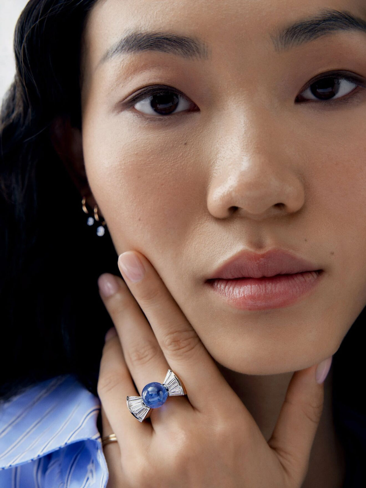 Close up of a model wearing a blue sapphire and diamond ring with bow shaped shoulders, showcasing Jessica McCormack craftsmanship and contemporary style View 3