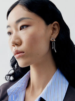 Close up portrait of a model wearing diamond and ribbon drop earrings with delicate dangling stones and a sculptural bow detail in a contemporary style