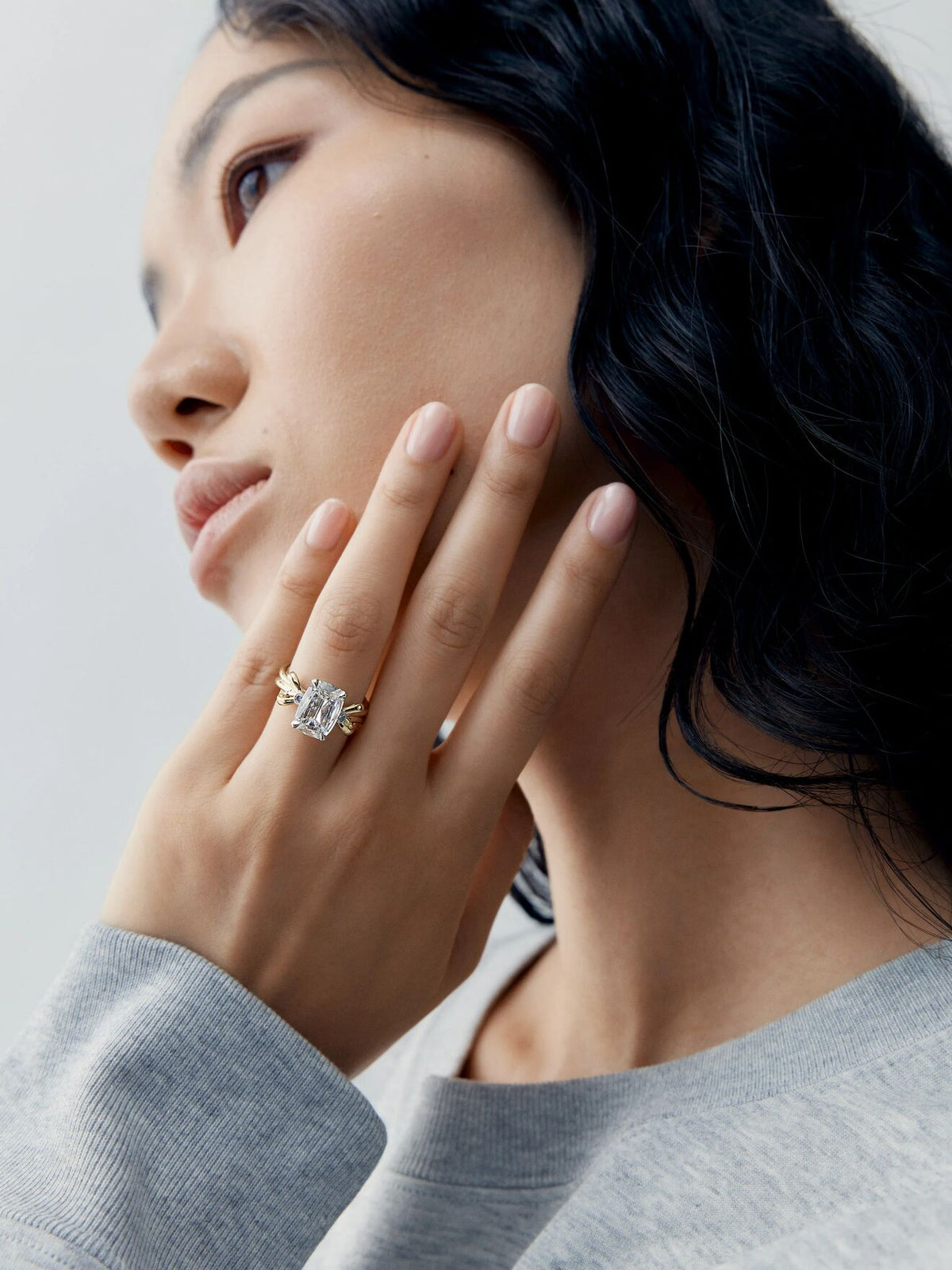 Jessica McCormack 3.01ct cushion cut diamond ring worn on a woman’s hand as she touches her face, showcasing a contemporary setting and refined craftsmanship View 3