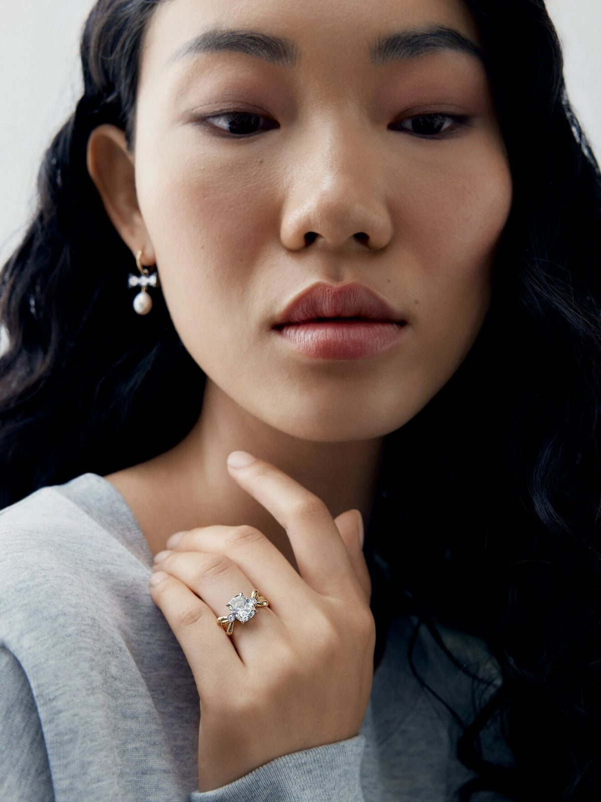 Close up portrait of a woman wearing a Jessica McCormack cushion cut diamond ring with a sculptural bow inspired setting and pearl drop earrings View 3