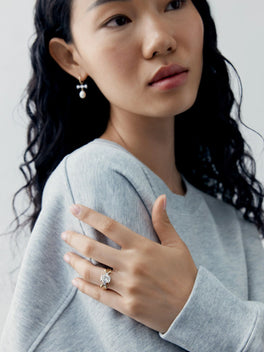 Woman wearing a cushion cut diamond ring with a distinctive bow-inspired setting, paired with a pearl drop earring and contemporary styling