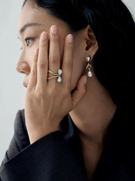 Woman wearing a pear shaped diamond and white gold ring with sculptural crossed bands, paired with a delicate drop earring
