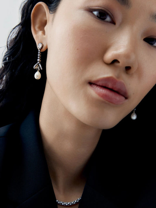 Close-up portrait of a model wearing asymmetric diamond and pearl drop earrings, featuring delicate diamond links and dangling pearls View 3