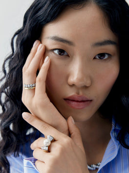 Portrait of a model wearing a pearl and diamond ring with an antique inspired setting alongside a diamond band by Jessica McCormack