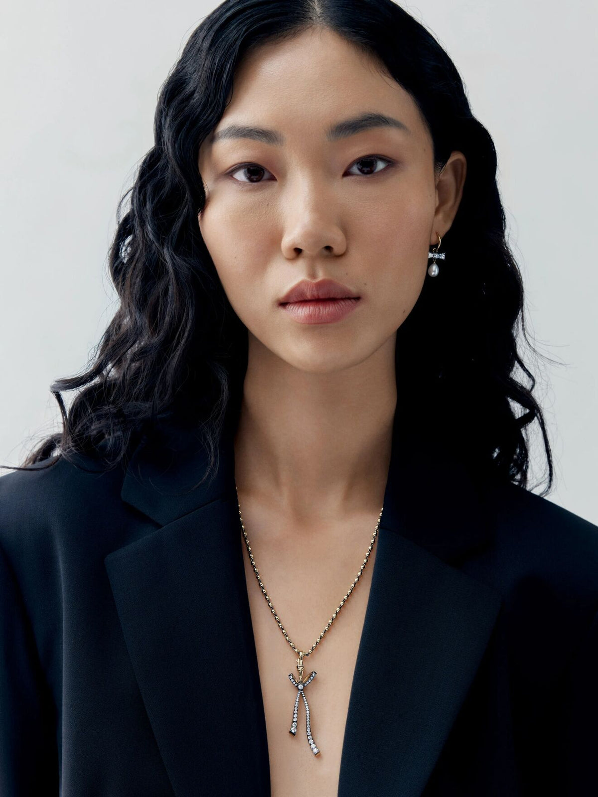Portrait of a woman wearing a diamond bow pendant on a delicate ball n chain necklace, styled with a contemporary black blazer View 3
