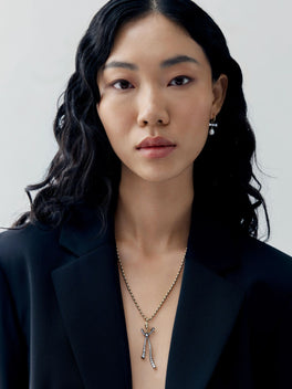 Portrait of a woman wearing a diamond bow pendant on a delicate ball n chain necklace, styled with a contemporary black blazer