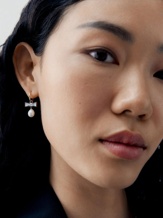 Close up portrait of a model wearing a diamond bow hoop earring with a dangling pearl in an antique inspired contemporary style by Jessica McCormack View 3