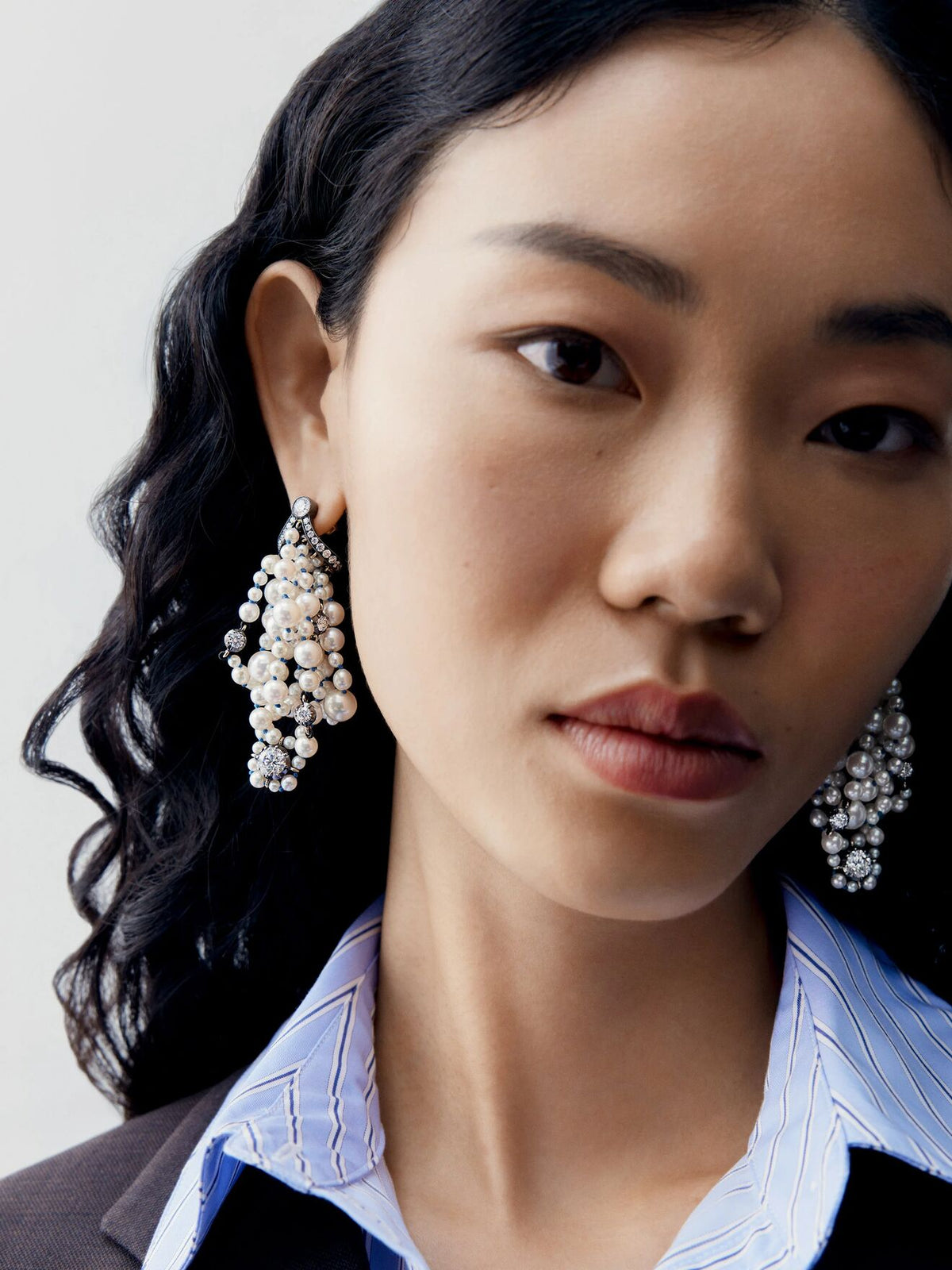 Close up portrait of a model wearing clustered diamond and pearl drop earrings with layered round stones and pearls in a contemporary statement design View 3