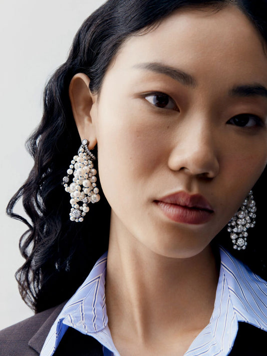 Close up portrait of a model wearing clustered diamond and pearl drop earrings with layered round stones and pearls in a contemporary statement design View 3