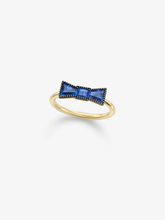 Yellow gold ring featuring a sculptural bow motif set with vivid blue sapphires and contrasting dark detailing on a white background