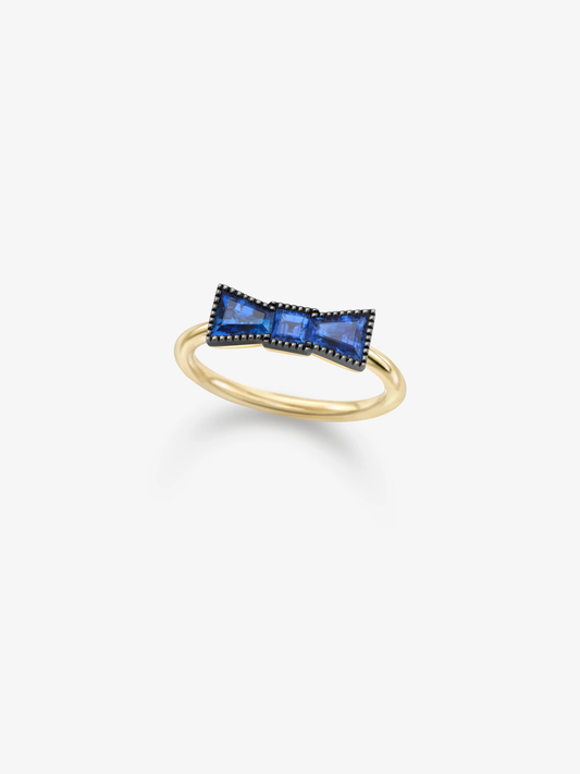 Yellow gold ring featuring a sculptural bow motif set with vivid blue sapphires and contrasting dark detailing on a white background View 2