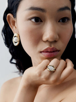 Close-up portrait of a woman wearing a twisted gold ring set with a 3.01ct oval diamond, showcasing contemporary style and traditional craft techniques