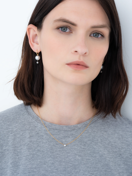Close-up of a woman wearing a delicate white gold pendant necklace with a small 0.25ct diamond, paired with elegant pearl and gold drop earrings, showcasing timeless craftsmanship.
