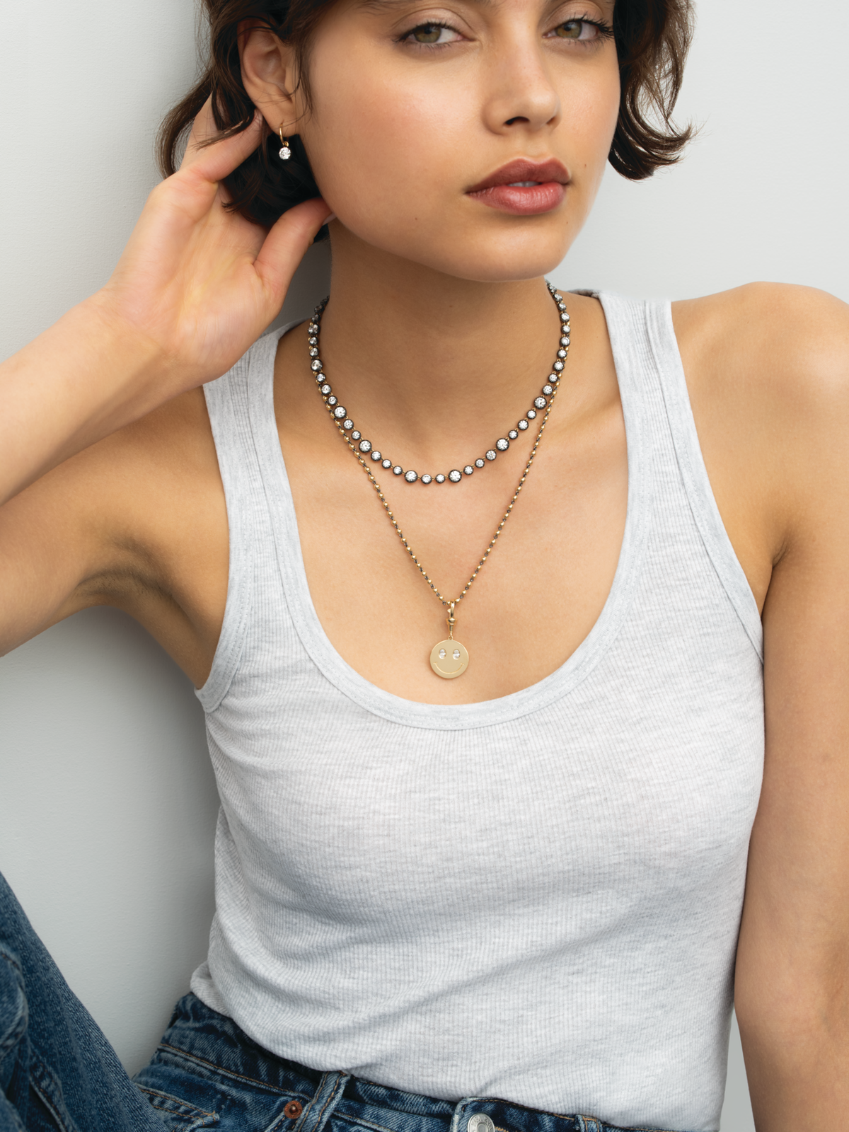 Model wearing layered necklaces with a diamond necklace and a round yellow gold happy face pendant by Jessica McCormack geschniegelt View 3